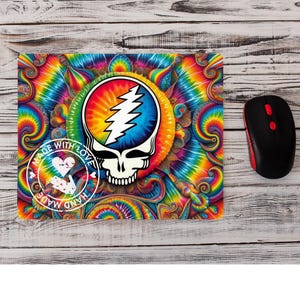 May include: A rectangular mousepad with a vibrant tie-dye design featuring a skull with a lightning bolt and the words "MADE WITH LOVE HAND MADE". A black and red computer mouse is next to the mousepad.