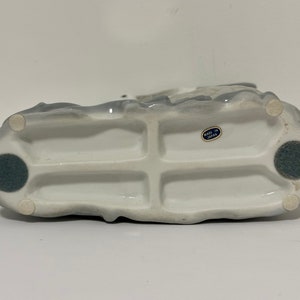 May include: White ceramic figurine with a gray glaze. The figurine has a detailed design and is marked "Made in Japan" on the bottom.