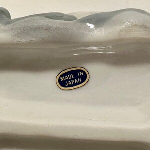 May include: White ceramic figurine with a blue label that reads "Made in Japan".