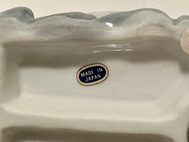 May include: White ceramic figurine with a blue label that reads "Made in Japan".