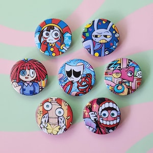 May include: A collection of seven round, colorful pinback buttons with cartoon illustrations. The designs feature various characters with unique expressions and styles, including a doll, a rabbit, and other whimsical figures. The buttons are arranged on a pink and green striped background.