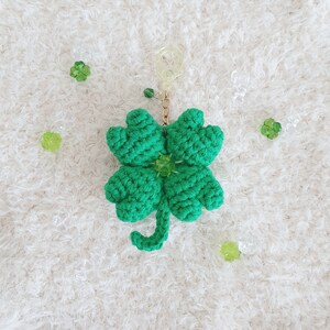 May include: A green crocheted four-leaf clover keychain with a gold chain and a green bead.