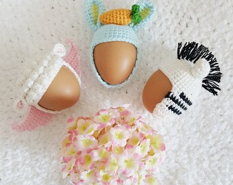 May include: Three Easter eggs decorated with crocheted bunny, zebra, and flower hats. The bunny hat is light blue with a carrot, the zebra hat is black and white, and the flower hat is white.
