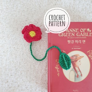 May include: Crochet bookmark pattern for Anne of Green Gables, featuring a red flower with a yellow center and a green leaf. The bookmark is shown on a red book with the title "Anne of Green Gables" in white text.