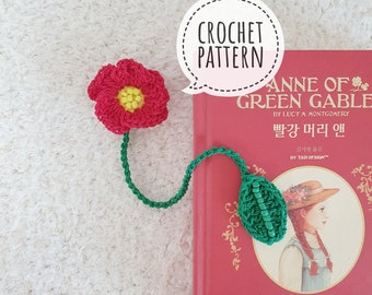Puede incluir: Patrón de marcapáginas de ganchillo para Ana de las Tejas Verdes, con una flor roja con un centro amarillo y una hoja verde. El marcapáginas se muestra en un libro rojo con el título "Ana de las Tejas Verdes" en texto blanco.