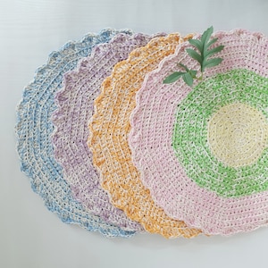 May include: Set of five crocheted placemats in pastel colours, including blue, purple, yellow, pink, and green. The placemats have a scalloped edge and a circular design.