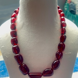 May include: A necklace made of deep red, faceted glass beads. The beads are oval shaped and have a glossy finish.