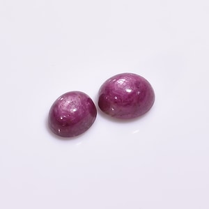 May include: Two round, cabochon cut, pink ruby gemstones. The stones are smooth and polished with a slight sparkle.
