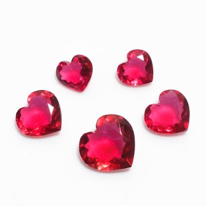 May include: Five red heart-shaped gemstones on a white background.