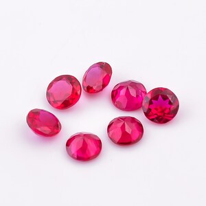 May include: Seven round, red gemstones with a faceted cut. The gemstones are arranged in a semi-circle on a white background.