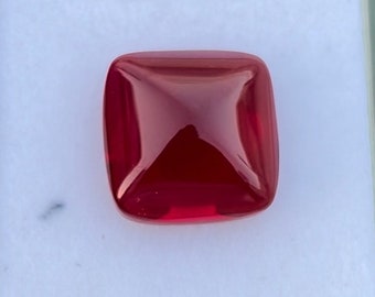 May include: A deep red gemstone with a square shape and a slightly domed top.