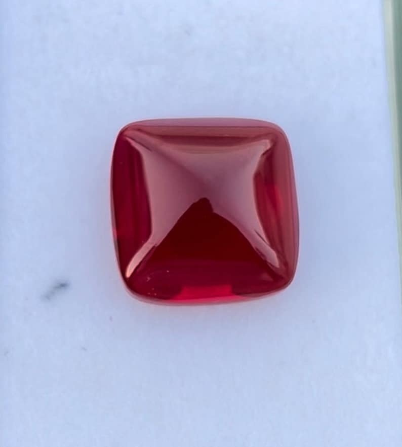 Pu&ograve; includere: Una pietra preziosa di colore rosso intenso con forma quadrata e parte superiore leggermente bombata.