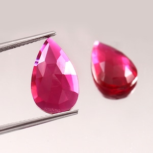 Op de afbeelding: Twee peervormige roze edelstenen, een vastgehouden door een pincet, met een facetgeslepen vorm en een hoogglans afwerking.