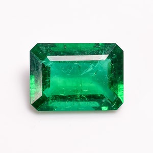 May include: A vibrant green emerald gemstone cut in a rectangular shape with facets.
