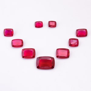 May include: Nine red gemstone cabochons in various sizes arranged in a semi-circle pattern on a white background.