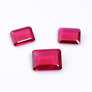 May include: Three red gemstone rectangular cut cabochons on a white background.