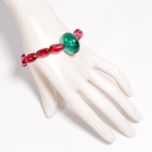 Peut inclure: Un bracelet composé de perles de verre roses et vertes. Le bracelet a une grosse perle verte de forme ovale au centre.