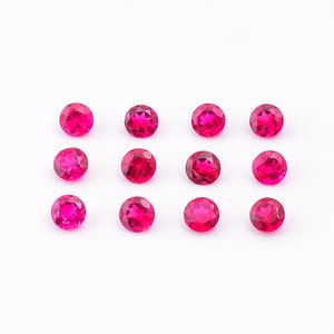 May include: Twelve round, faceted, ruby red gemstones arranged in three rows of four on a white background.