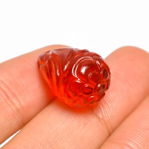 以下が含まれることがあります： 彫刻された、半透明のオレンジレッドの宝石。 宝石は手で持たれており、片方の端に詳細な花の模様があります。 石は滑らかで磨かれた外観をしており、装飾品またはジュエリーコンポーネントである可能性があります。