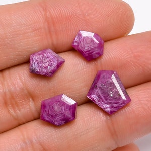 Puede incluir: Cuatro piedras preciosas de rubí rosa facetadas con forma hexagonal. Las piedras preciosas están dispuestas en una mano.