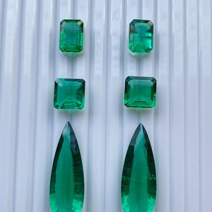 Può includere: Quattro pietre preziose di colore verde smeraldo, due quadrate e due a forma di lacrima, disposte a coppie su uno sfondo bianco.