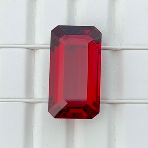 May include: A deep red, emerald-cut gemstone with a high polish.