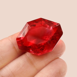 May include: A deep red gemstone with a faceted cut, resembling a ruby.
