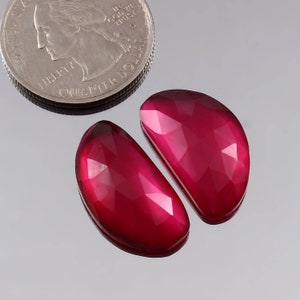May include: Two red gemstone cabochons, each shaped like a half-moon, with a faceted surface.