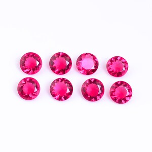 May include: Eight round, faceted, pink gemstones on a white background.