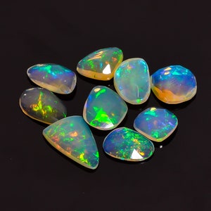 Peut inclure: Une collection de huit pierres précieuses d'opale irisées, chacune avec un motif unique de teintes vertes, bleues et jaunes. Les pierres sont taillées dans une variété de formes, notamment ovale, poire et ronde.