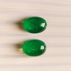 Puede incluir: Dos piedras preciosas verdes de forma ovalada sobre un fondo blanco.