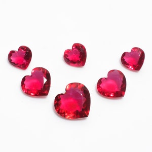 May include: Six red heart-shaped gemstones on a white background.