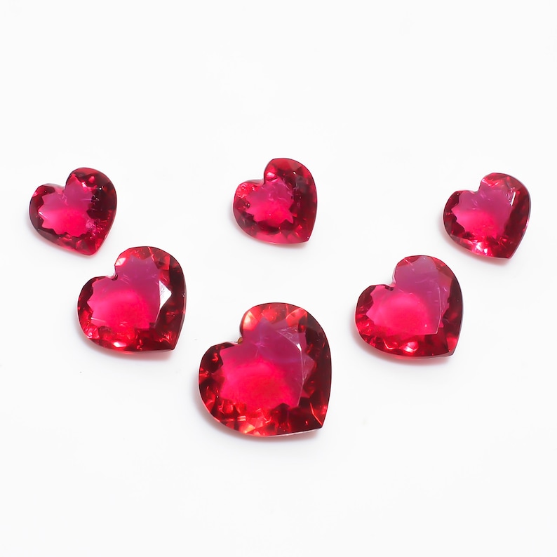 May include: Six red heart-shaped gemstones on a white background.