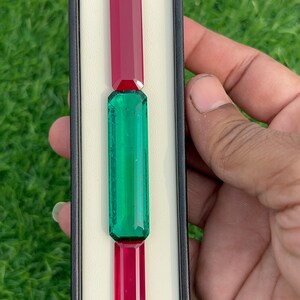 May include: Three rectangular gemstones displayed in a black and white box. The top and bottom gemstones are red, and the middle gemstone is green.