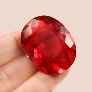 Könnte beinhalten: Ein großer, ovaler, roter Edelstein mit Facettenschliff. Der Edelstein wird in einer Hand gehalten.