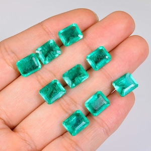 May include: Nine emerald green gemstones, cut into rectangular shapes, are displayed on a hand. The gemstones are all approximately the same size and have a smooth, polished finish.