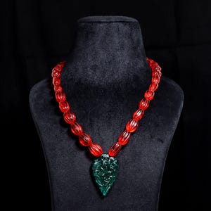 May include: A red beaded necklace with a carved green gemstone pendant in the shape of a heart.