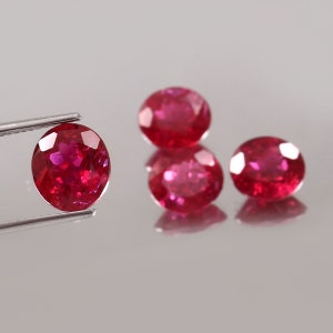 May include: Four round, red gemstones with a faceted cut. The gemstones are displayed on a white surface.