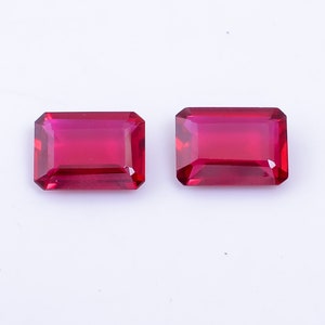 May include: Two red gemstone rectangular cut cabochons on a white background.