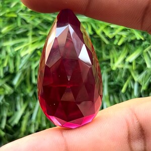 Puede incluir: Un colgante de cristal facetado en forma de lágrima de color rojo oscuro.