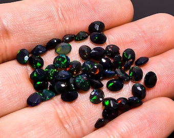 Puede incluir: Una colección de piedras preciosas de ópalo negro con destellos iridiscentes verdes y rojos. Las piedras preciosas son de forma ovalada y tienen un acabado liso y pulido.