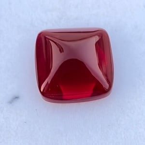 Pu&ograve; includere: Una pietra preziosa quadrata di colore rosso scuro con una superficie lucida e sfaccettata.