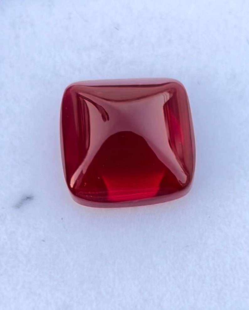Pu&ograve; includere: Una pietra preziosa quadrata di colore rosso scuro con una superficie lucida e sfaccettata.