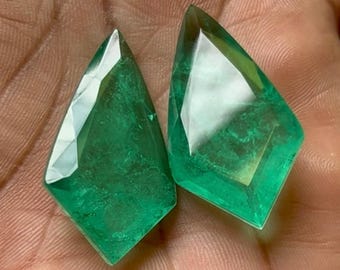 Puede incluir: Dos cabujones de piedra preciosa verde esmeralda cortados en forma de cometa. Las piedras preciosas son facetadas y tienen una apariencia translúcida.