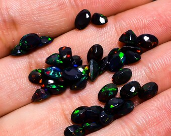 May include: A collection of oval-shaped black opals with iridescent green, blue, and red flashes. The opals are loose and scattered on a hand.