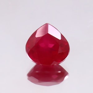 Puede incluir: Una piedra preciosa de color rojo intenso en forma de pera con un corte facetado.