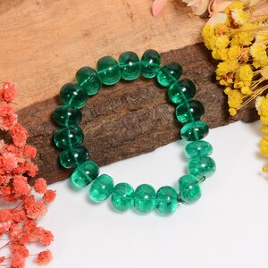 May include: A green glass bead bracelet with a rounded shape. The beads are translucent and have a slight sparkle.