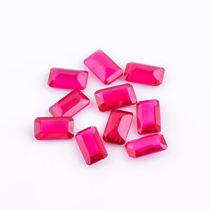 Könnte beinhalten: Zehn facettierte, rechteckige, rote Edelsteine. Die Edelsteine sind auf einer weißen Oberfläche verstreut.