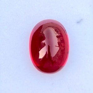 May include: A smooth, oval-shaped, red gemstone with a high polish.