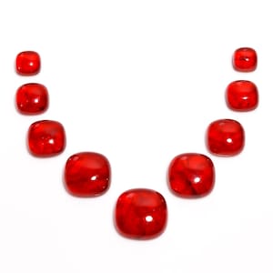 May include: A collection of ten square-shaped, polished red gemstones arranged in a curved line. The stones vary slightly in size and have a glossy, translucent appearance, with internal marbling.